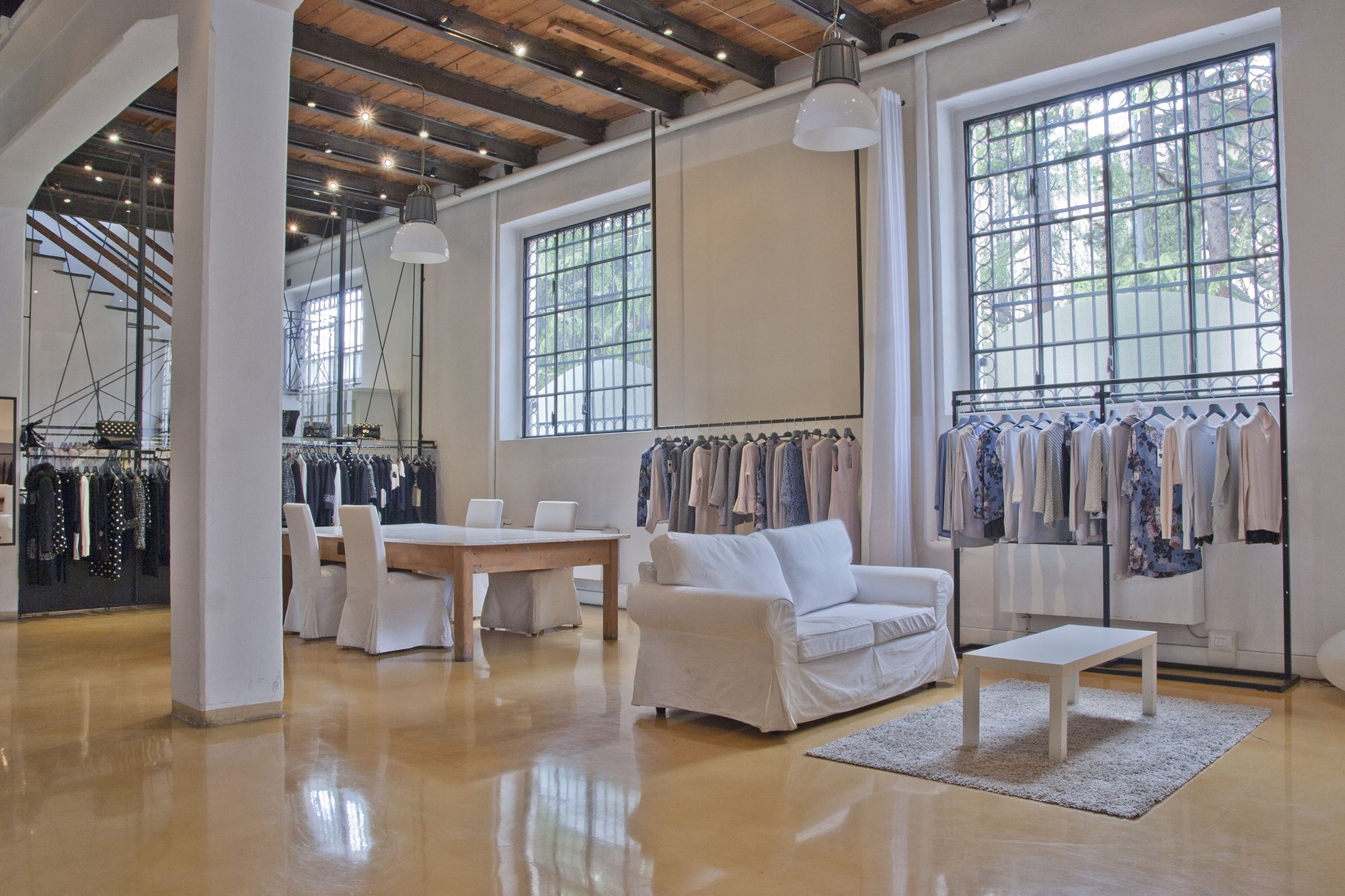 Sala dello showroom Olimpia D. con le collezioni esposte, finestre ad arco e travi in legno